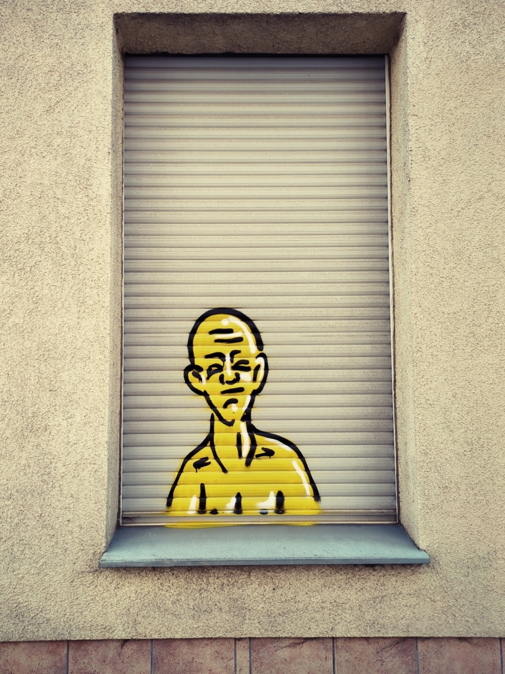 Graffiti (Graffito?) eines gelben Männchens im Comicstil auf einem geschlossenen Rolladen.