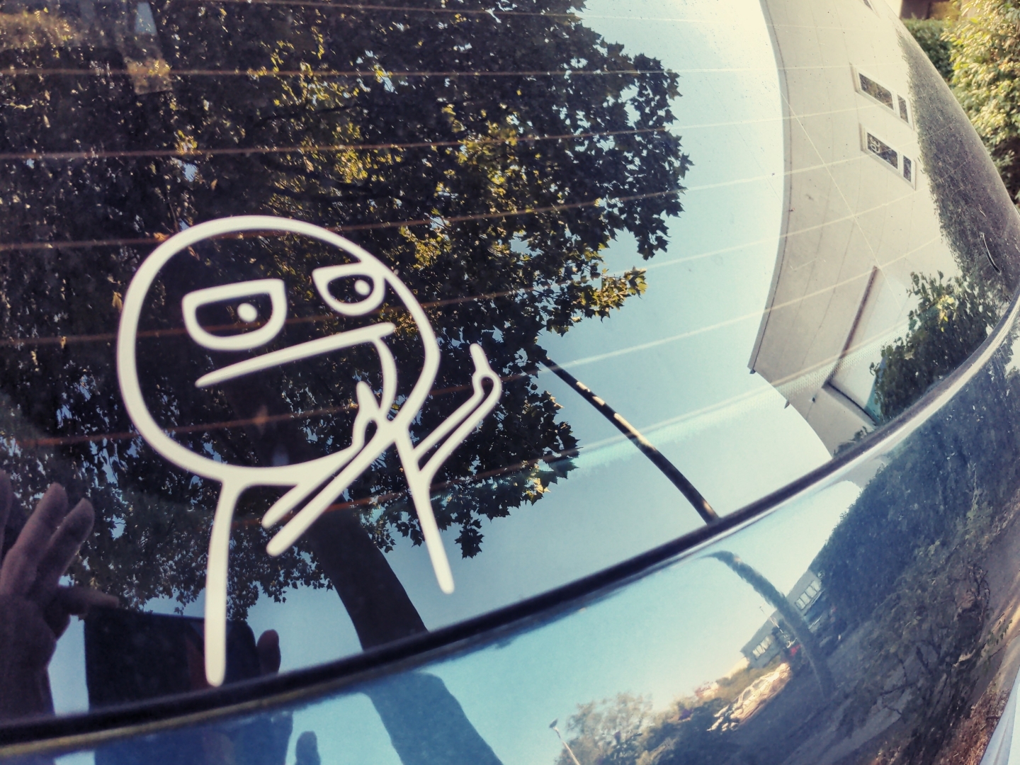 Aufkleber auf einer Autoheckscheibe. Eine Comicfigur zeigt mit beiden Händen den Mittelfinger.