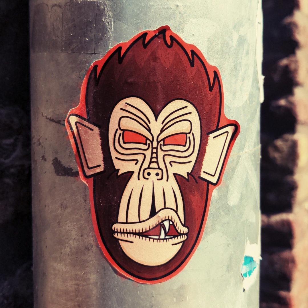 Aufkleber auf einem Regenrohr. Motiv ist ein Gorillagesicht als Comic.