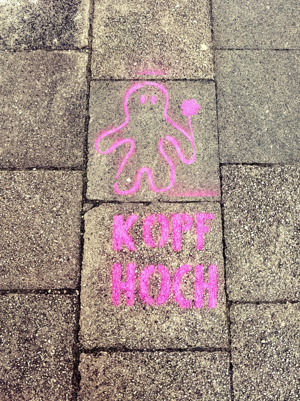 Graffiti auf einem Gehweg. Silhouette eines Wesens mit Luftballon, Schriftzug "Kopf hoch".